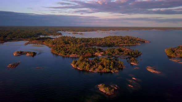 Small Rocky Islands with Green Pine Trees in Clear Blue Lake at Sunset, Drone Aerial Wide Orbit. Fly