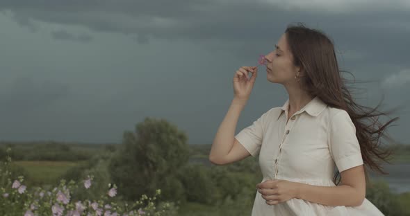 Side Portrait of Girl Smelling Wild Flower Outdoors on Stormy Sky Country Background. Beautiful