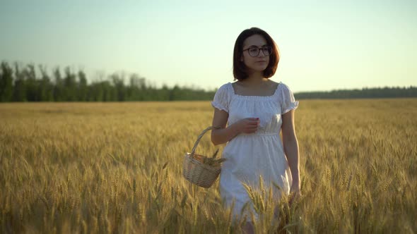 A Young Woman Is Walking on a Yellow Wheat Field with a Basket in Her Hands. Straw Basket with