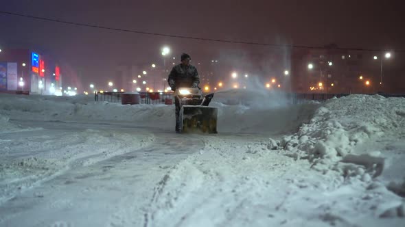 Snow Removal with a Snow Thrower in the Evening in an Amusement Park