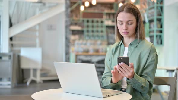 Professional Woman Using Smartphone and Laptop in Cafe