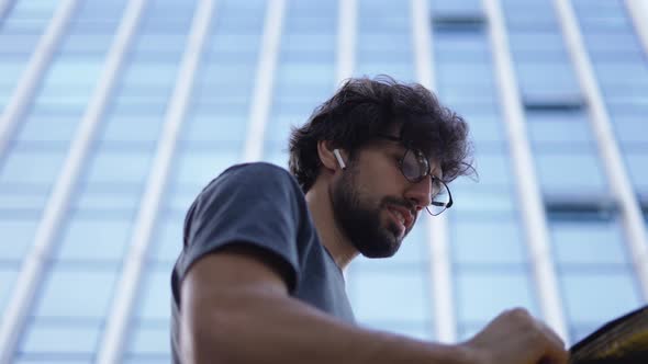 Delivery Man with Yellow Backpack Talk to a Client on the Street Using Earphones Low Angle View