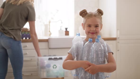 Portrait video of smiling girl holding plastic bottles in kitchen.