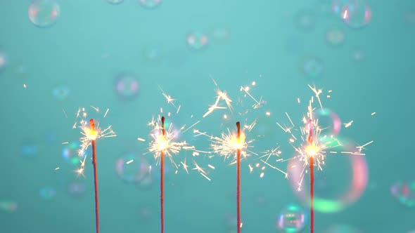 Sparklers Burn and Sparkle Against Blue Background with Flying Rainbow Soap Bubbles