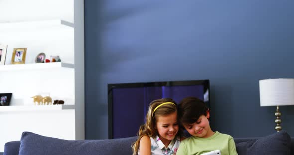 Siblings using digital tablet in living room