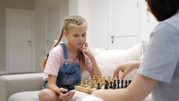 Mother and Daughter Playing Chess and Sitting on a Sofa in Living Room