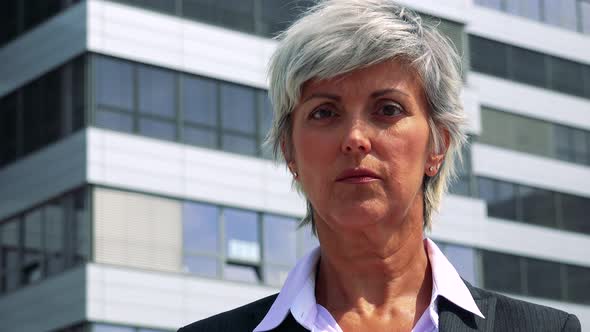 Business Middle Age Woman Looks To Camera with Serious Face - Company Building