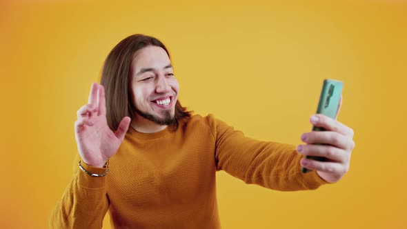 Cheerful Bearded Caucasian Man with Long Hair Looking at His Smartphone and Talking to Someone Via