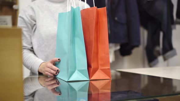 Unrecognizable Young Woman Passing Shopping Bags To Client at Cash Desk in Store. Caucasian Female