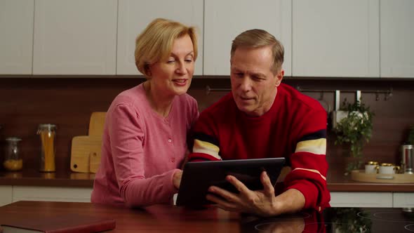 Happy Attractive Mature Couple Web Surfing with Tablet Pc in Domestic Kitchen