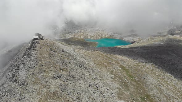 Aerial: flying over high altitude landscape, rocky mountain peaks and blue alpine lake