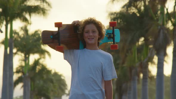 Happy Care Free Boy Skateboarding Down Street at Sunset with Hands Up in Air