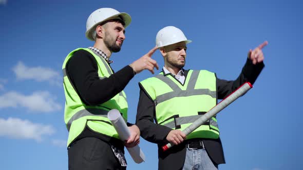 Two Smart Positive Young Men in Hard Hat and Uniform Gesturing Highfive Discussing Building at