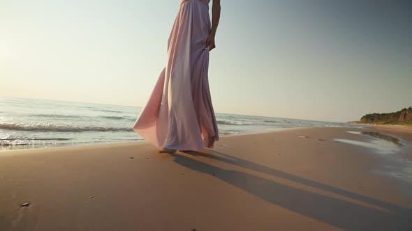 Follow Dolly Out Pretty Woman in Long Dress Walking on Wet Sand Against Sunset Sea Background