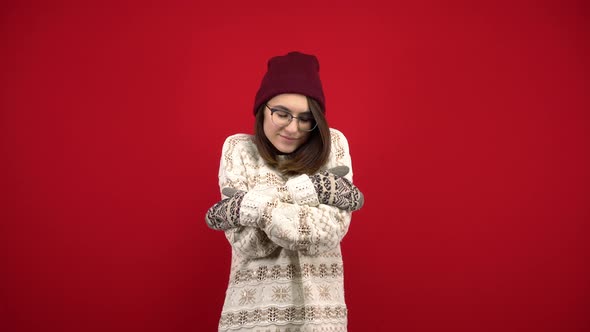 A Young Woman Wearing Glasses, a Hat and Mittens Is Cold and Hugs Herself To Keep Warm. Shooting in