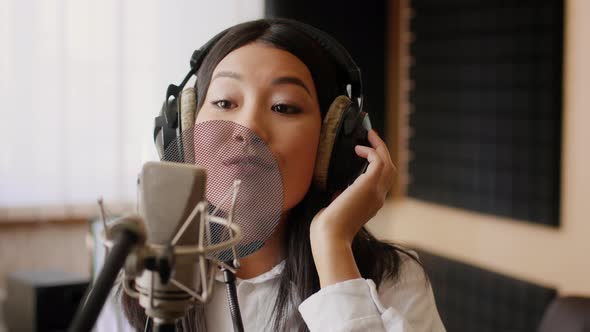 Energetic Young Asian Female Vocalist Singing In Microphone In Music Studio