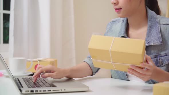 Asian young woman owner of SME online check product on stock and save to computer working at home.