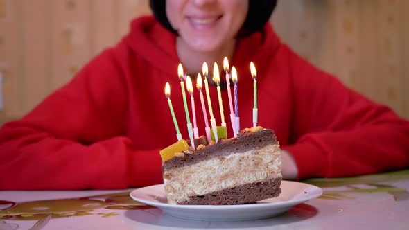 A Happy Girl Looks at Burning Candles on a Piece of Birthday Chocolate Cake