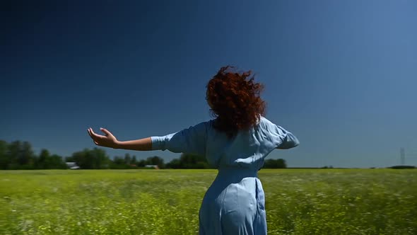 Caucasian Young Woman in a Blue Dress Dances in a Field