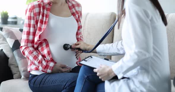Doctor Listens with Stethoscope to Belly of Pregnant Woman at Home