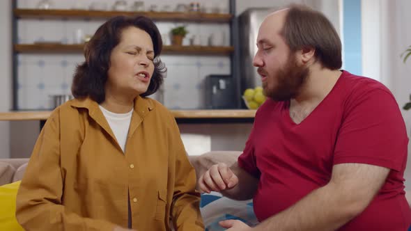 Young Man Helping Senior Mother with Heart Attack Sitting on Couch