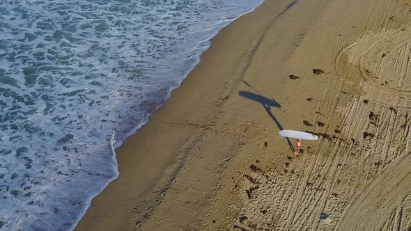 Aerial drone uav view of a surfer walking with his sup surfboard.