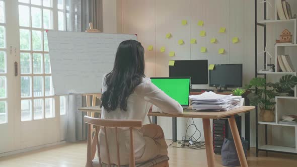 Back View Of Asian Woman Talking To Green Screen Laptop While Working With Documents At The Office