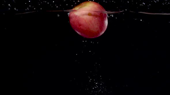 Vibrant red apple being dropped into water in slow motion.