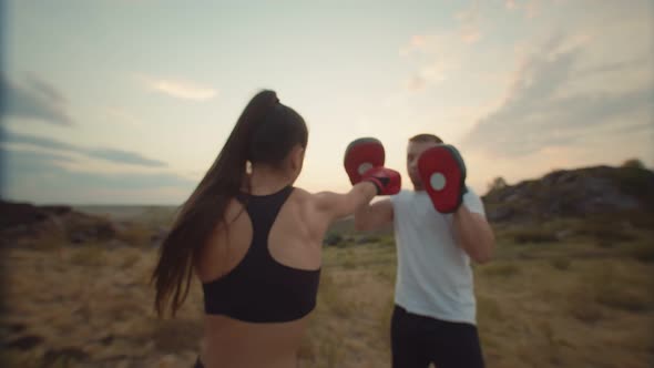Woman in Boxing Gloves Hits the Paws Held By Trainer in Nature View From the Back
