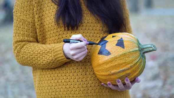 Close Up Woman Hands Paint Orange Pumpkin with Black Paint in Autumn Forest