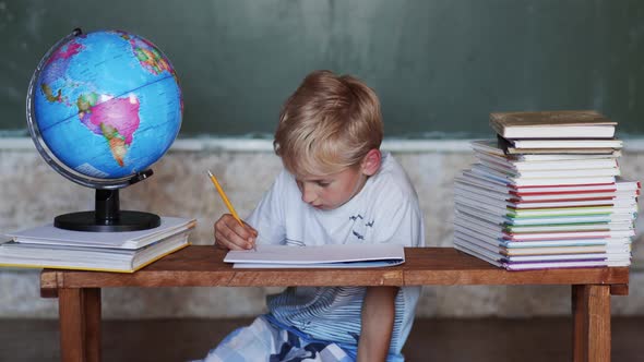 A Boy of 8 Years Old Does Homework Against a Background of the Globe. Home School Concept.