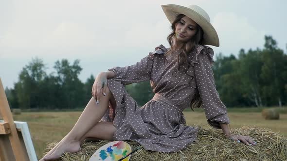 Creative artist outside in field on sunset sits on haystack admiring picture