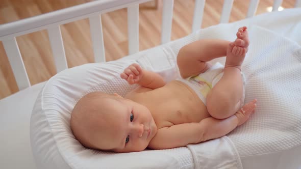 a Small Newborn Baby Lies in a White Bed in a Diaper Moves His Legs