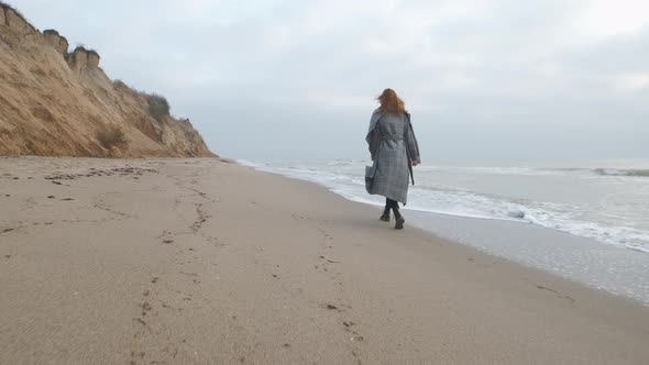 Attractive Redhead Woman in Coat Walking on the Wild Autumn Beach