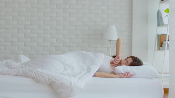 Asian young woman wake up and stretching her arms in white cozy bedroom in the morning