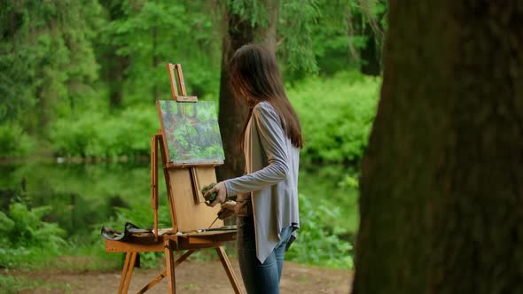 Rear Middle View of a Young Artist Woman Painting a Landscape in a Summer Forest
