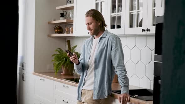 A Man is Texting and Surfing the Net on His Phone in the Kitchen