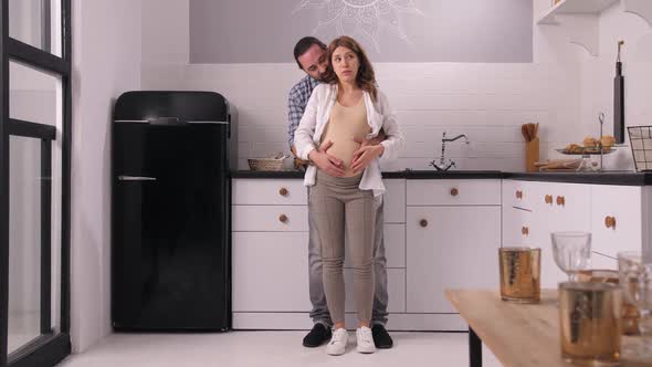 Joyful Pregnant Couple Stroking Belly in Kitchen