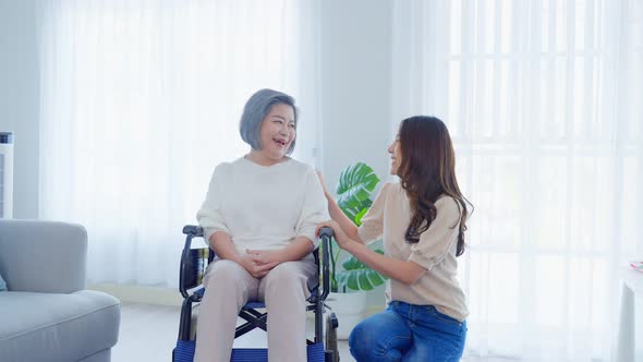 Asian young daughter support and take care older disabled woman on wheelchair at home.