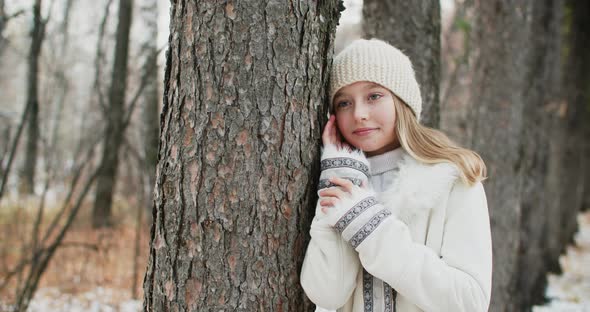 Romantic Woman in White Jacket and Knitted Hat Leaned on Tree Trunk Posing for Shooting