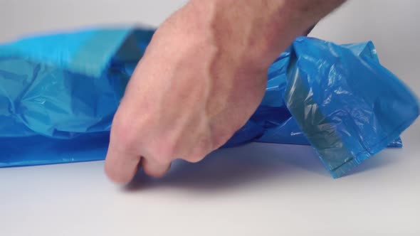Man opens a new plastic blue garbage bag 