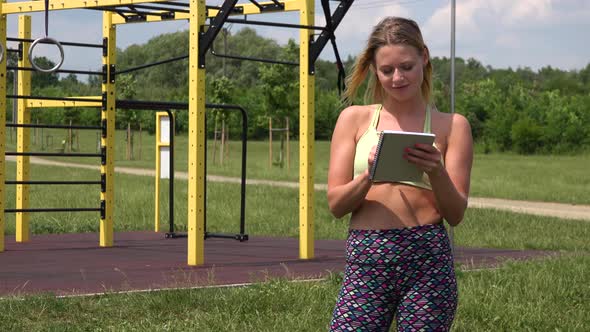 A Fit Beautiful Woman Writes Into a Notebook at an Outdoor Gym