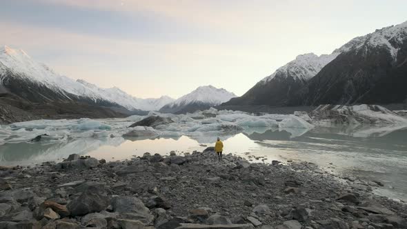 Wide angle shot of woman walking up to the edge of the glacial Tasman Lake in New Zealand on a cold