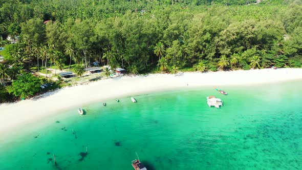 Boats floating on shallow turquoise lagoon near sandy beach bordered by palm trees and tropical rain