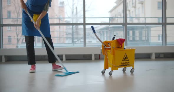 Uniformed Cleaner Wiping Floor Using Mop and Cart in Business Center