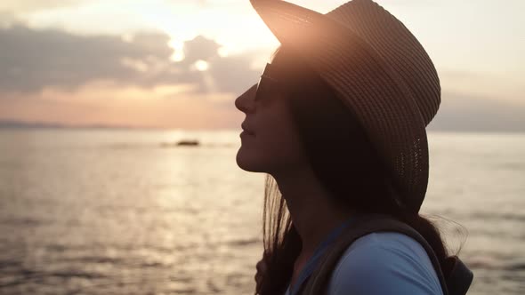 Closeup Smiling Travel Woman in Sunglasses Putting on Hat Admiring Amazing Sea Landscape at Sunset