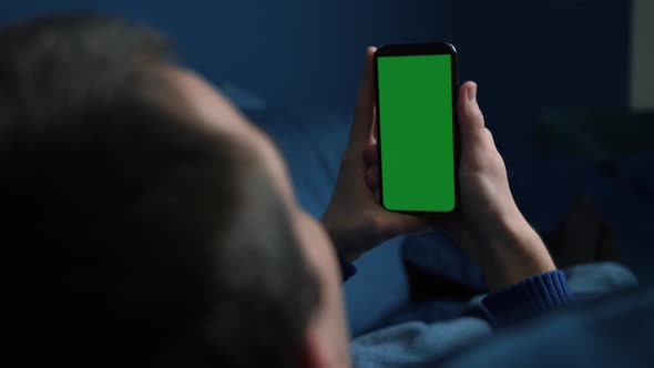 Man Lying on Couch Using Smart Phone with Chroma Key Green Screen at Night, Scrolling Through Social