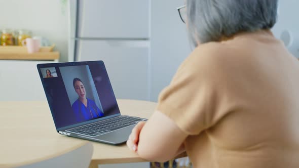 Asian senior older woman video call with doctor in living room at home.