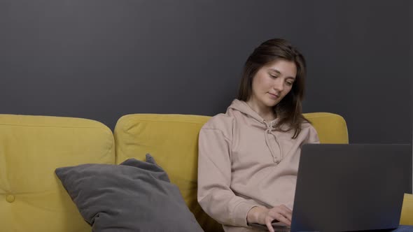 Young Lady Holds Tablet Communicating on Social Networks on Sofa in Cozy Room
