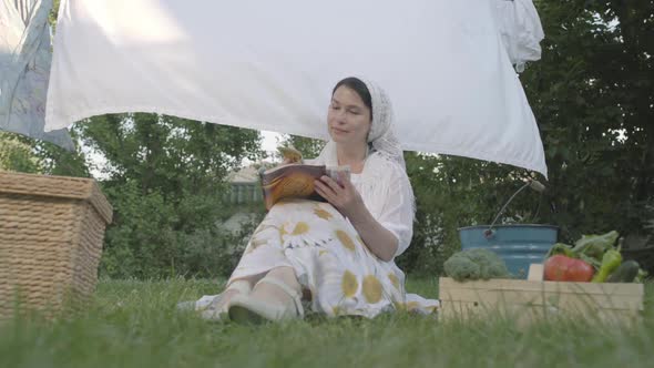 Adorable Woman with a White Shawl on Her Head Resting in the Garden Sitting on the Grass